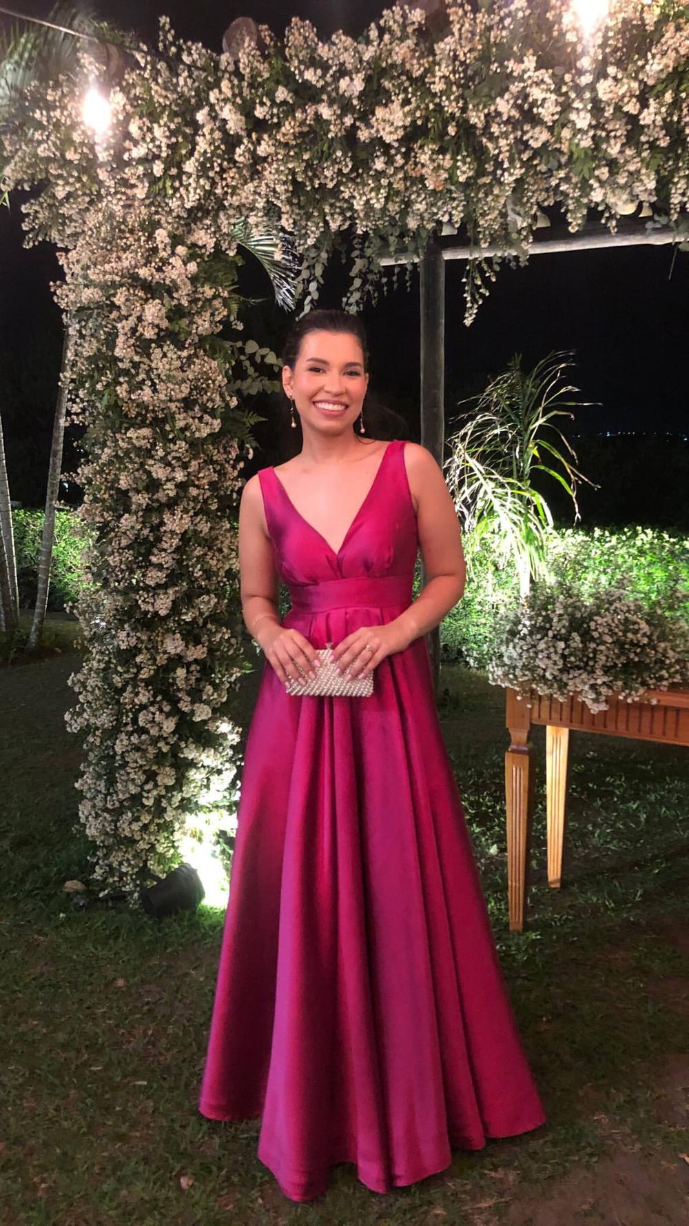 Vestido longo fúcsia de tecido encorpado, com decote V, cintura marcada e saia ampla evasê.
