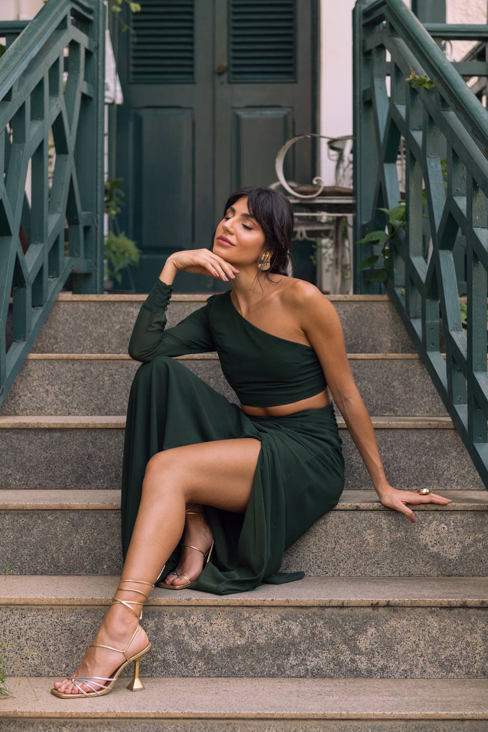 Vestido longo verde escuro de um ombro só, com manga longa, recorte na cintura e saia fluida com fenda.