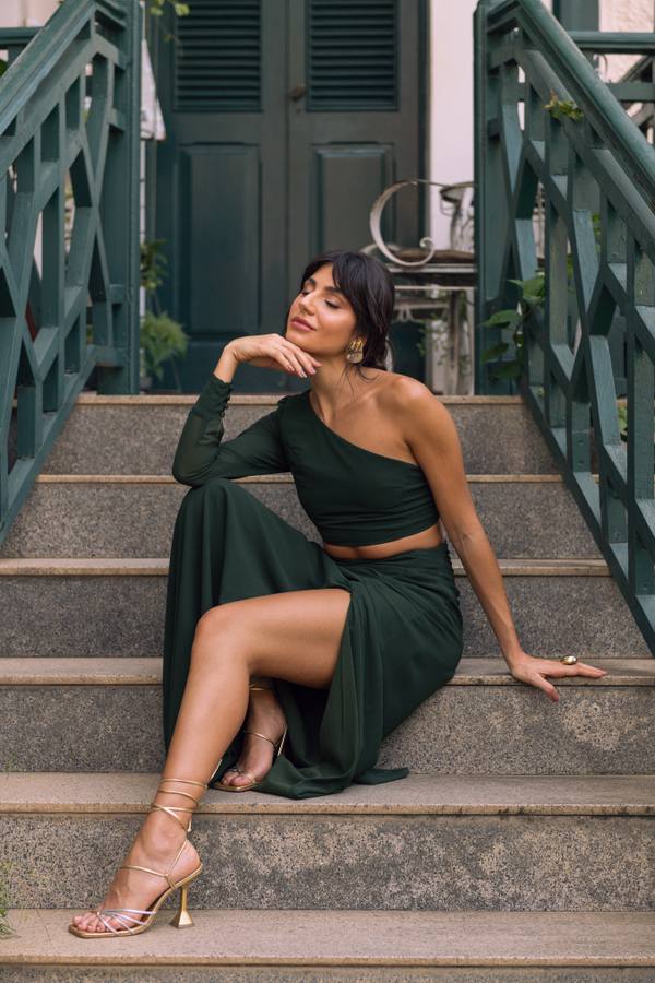 Vestido longo verde escuro de um ombro só, com manga longa, recorte na cintura e saia fluida com fenda.
