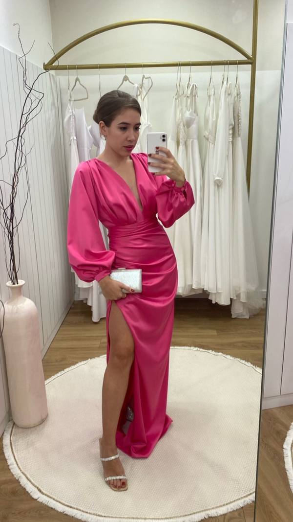 Vestido longo fúcsia em cetim, com mangas longas bufantes, decote V profundo e fenda lateral alta.