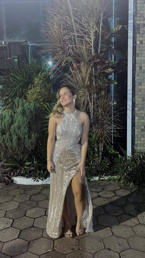 Vestido longo champagne com paetês, decote frente única, modelagem reta e fenda frontal destacada.