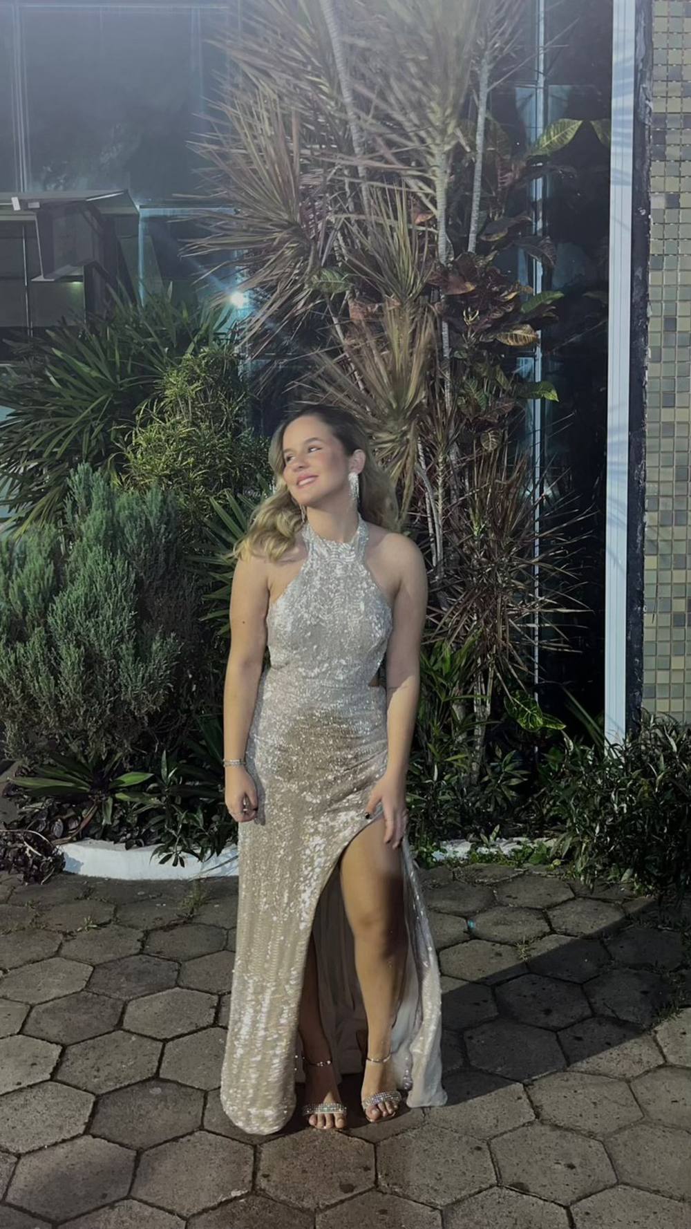 Vestido longo champagne com paetês, decote frente única, modelagem reta e fenda frontal destacada.