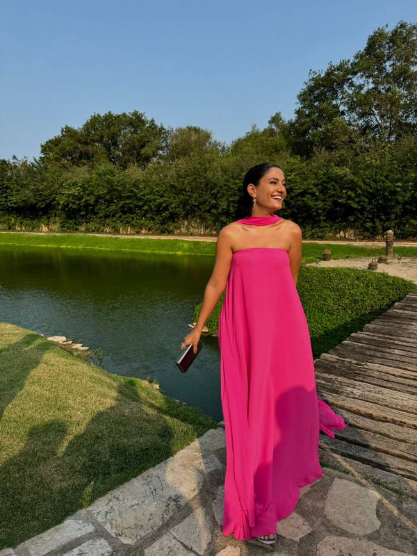 Vestido longo fúcsia tomara que caia com caimento fluido e detalhe de faixa no pescoço.