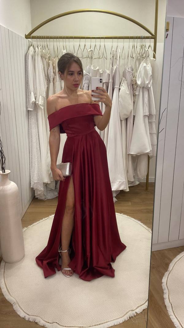 Vestido longo marsala em cetim com decote ombro a ombro, fenda alta na saia e caimento fluido.