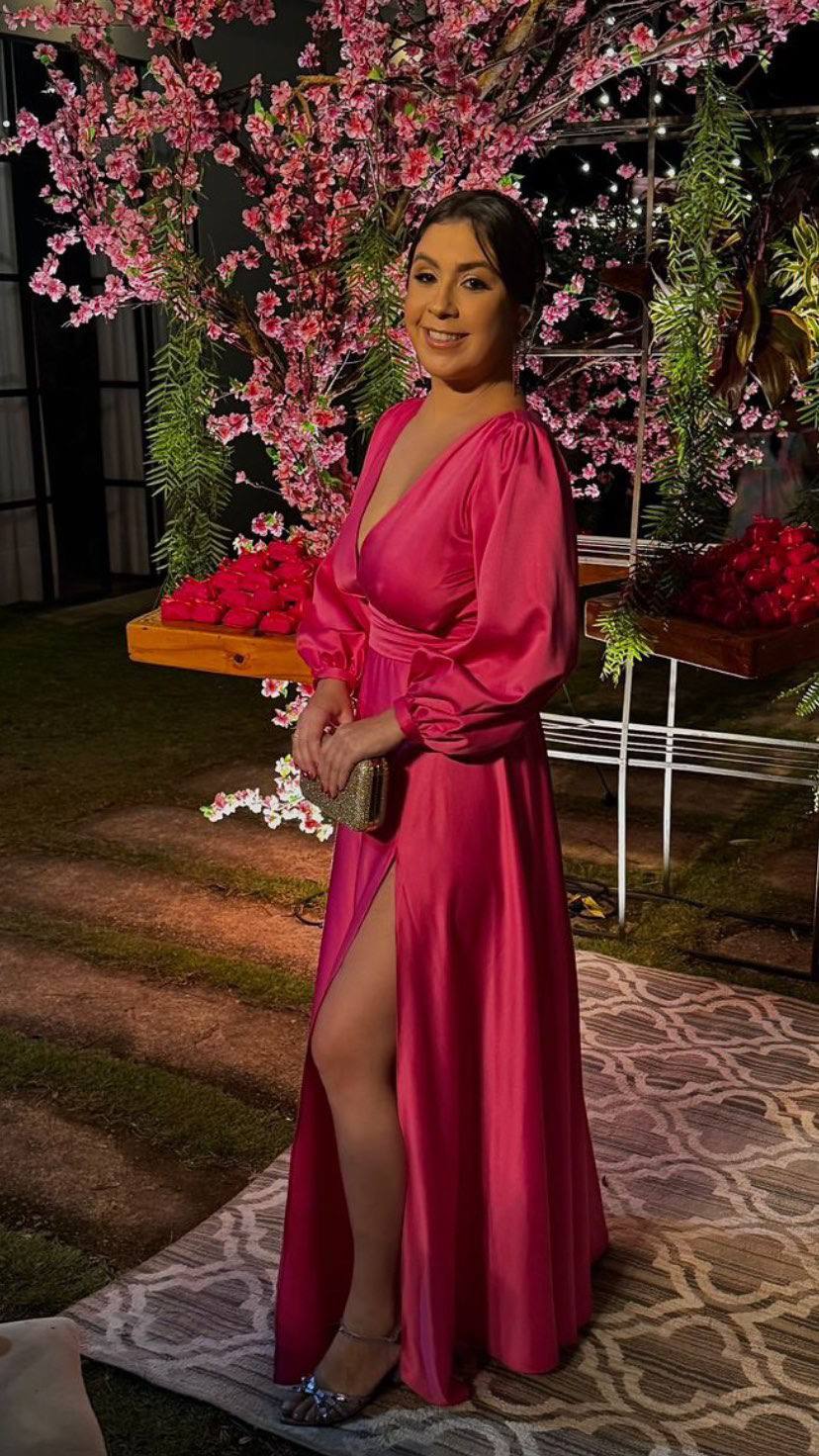 Vestido longo fúcsia em cetim, de mangas longas, decote V, caimento fluido e fenda na saia.