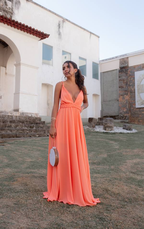 Vestido longo coral em tecido fluido, com decote V profundo, alças finas e detalhe trançado na cintura.