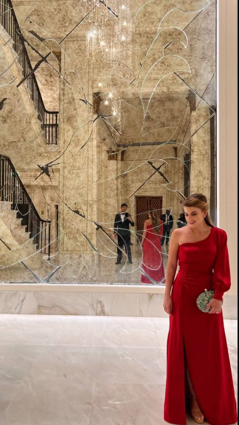 Vestido longo vermelho de um ombro só com uma manga longa, caimento fluido e fenda frontal.