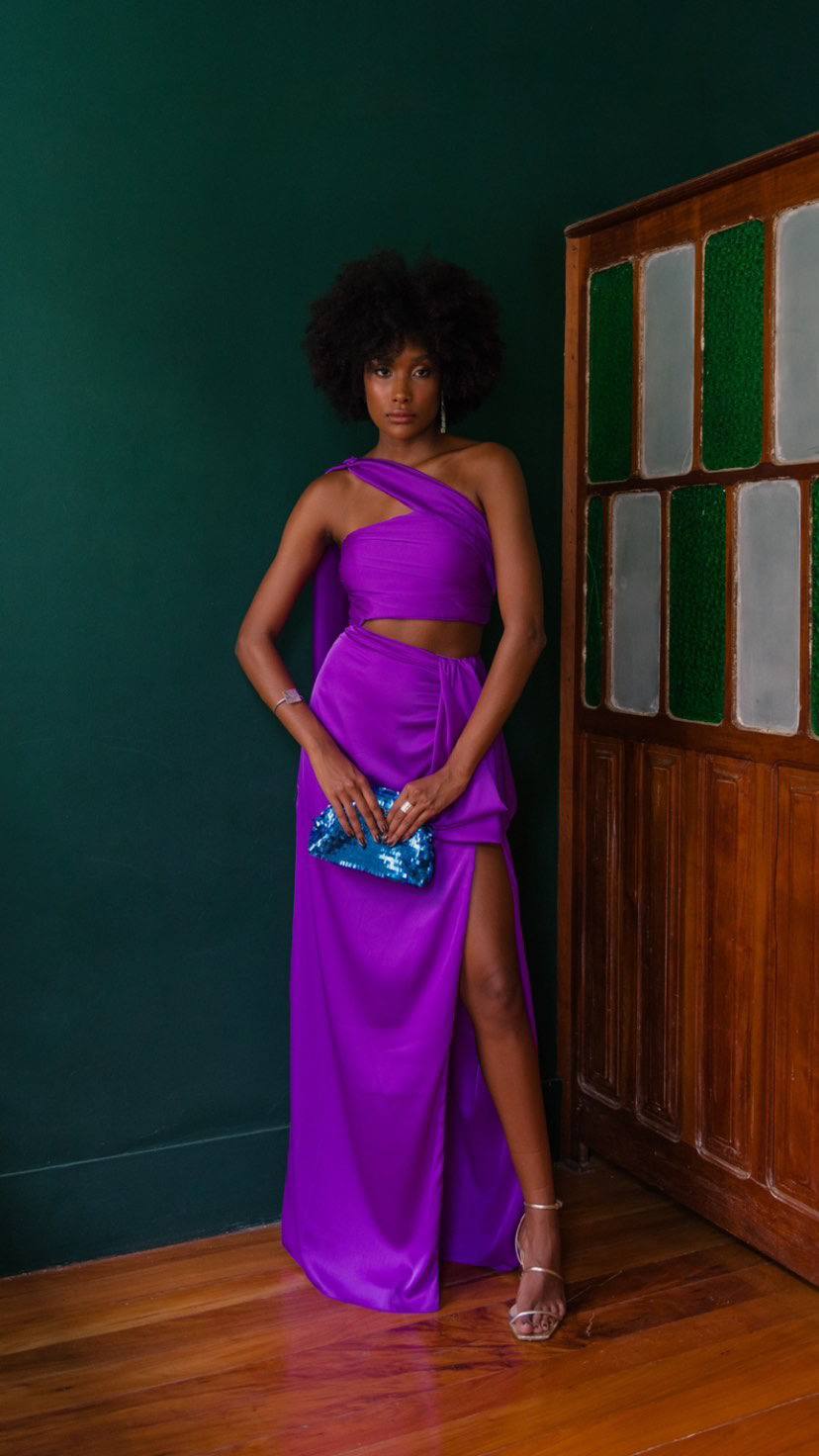 Vestido longo roxo de um ombro só, com recorte na cintura, saia com fenda lateral e caimento fluido.