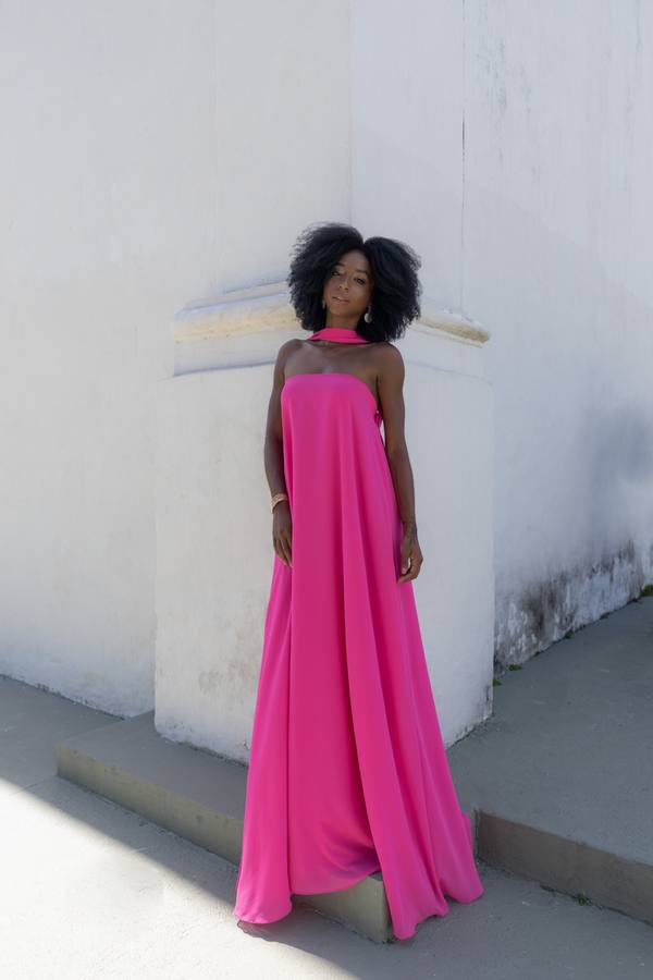 Vestido longo fúcsia de caimento fluido, decote tomara que caia e detalhe de faixa no pescoço.