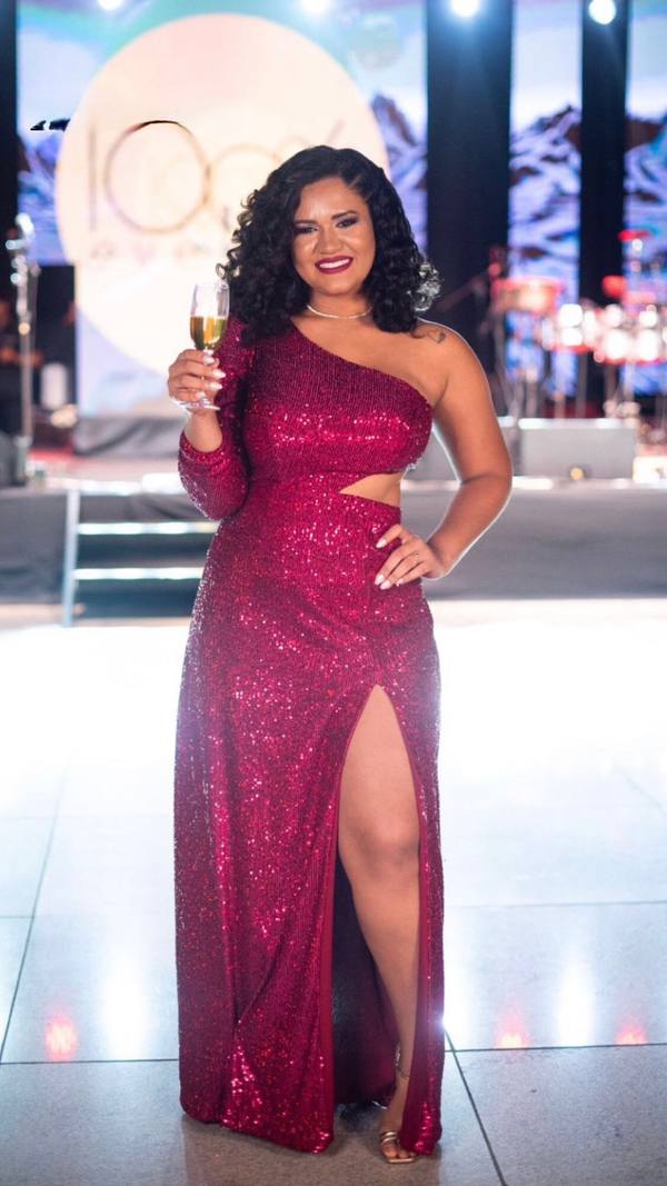 Vestido longo fúcsia de paetês, com recorte na cintura, fenda profunda na saia e modelo de um ombro só.