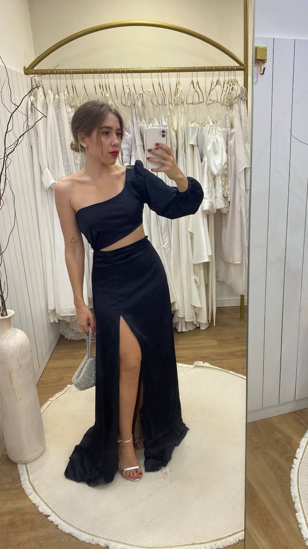 Vestido longo preto de um ombro só, com manga longa bufante, recorte na cintura e fenda frontal.