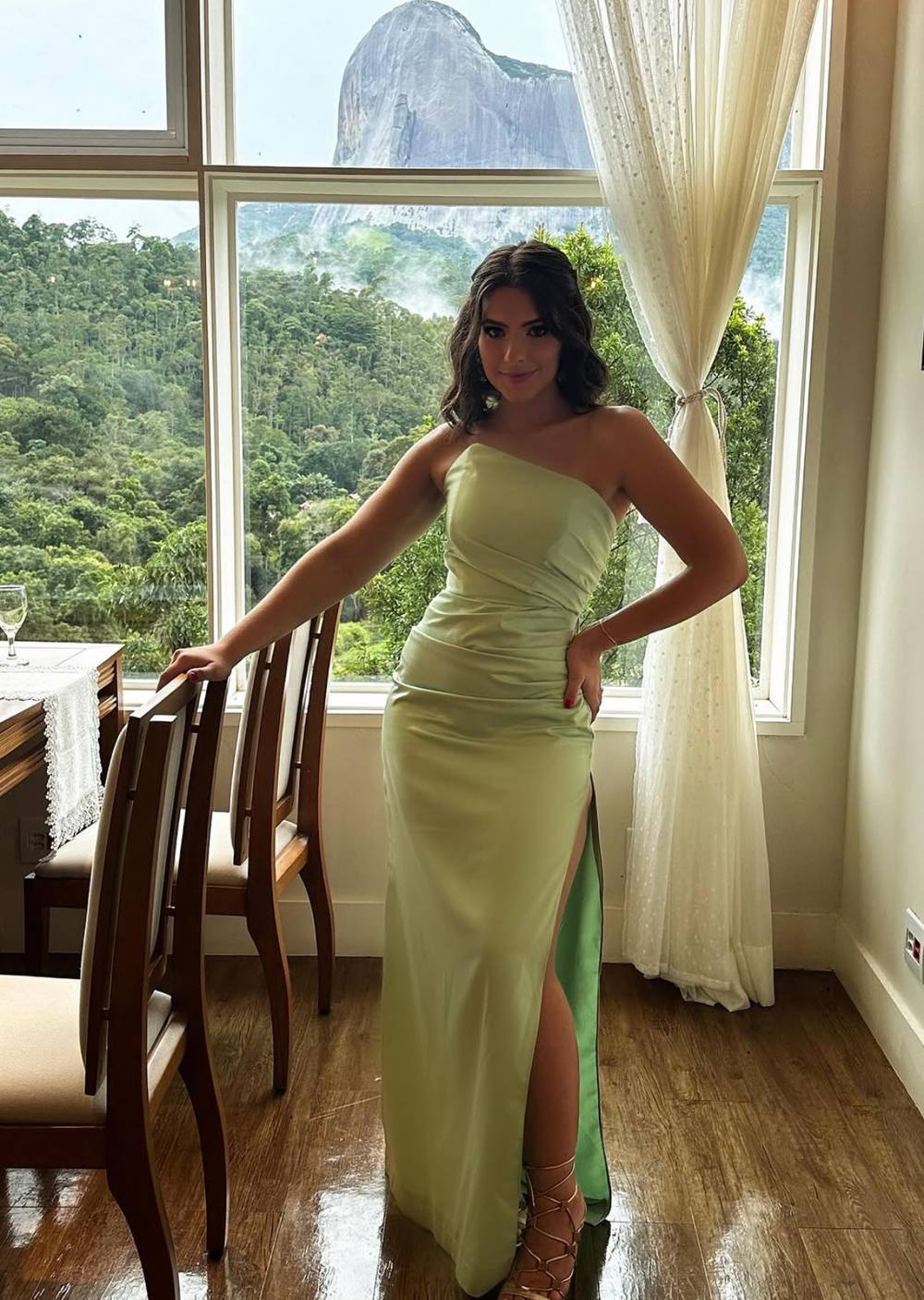 Vestido longo verde claro em cetim, decote tomara que caia assimétrico, caimento reto com fenda lateral.