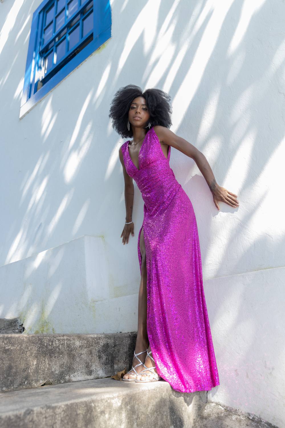 Vestido longo fúcsia de paetê com decote V, fenda alta na saia e caimento reto.