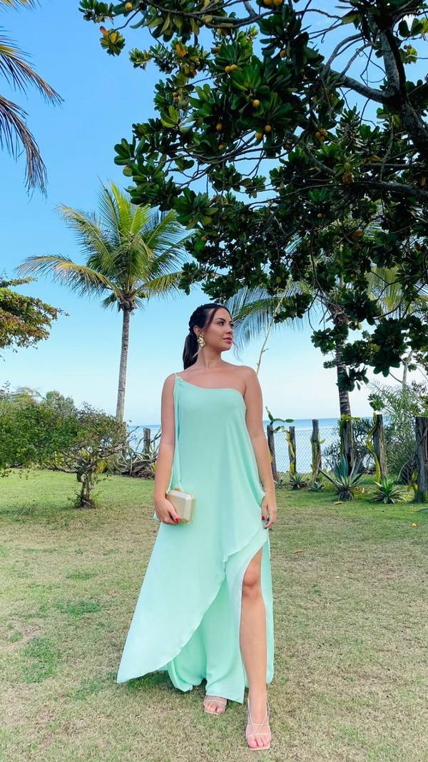 Vestido longo verde claro, modelo um ombro, tecido fluido e leve com fenda lateral.