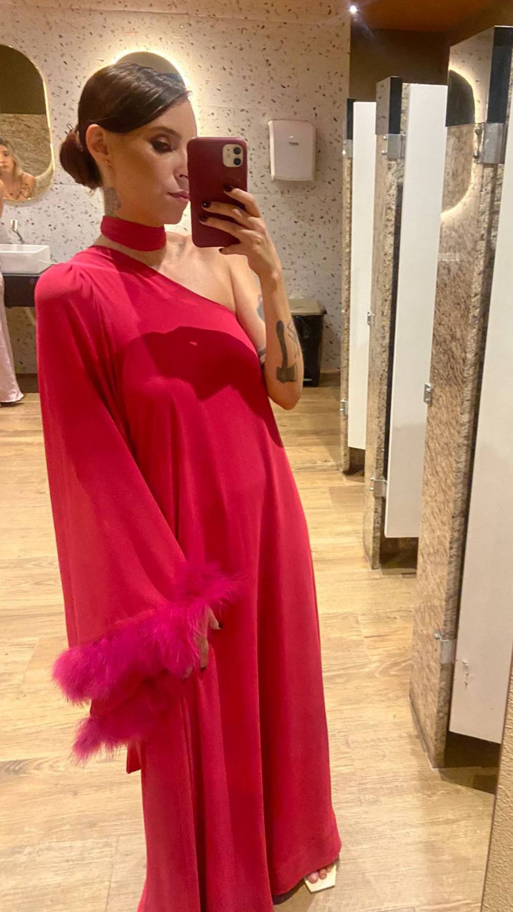 Vestido longo fúcsia de um ombro só, modelagem fluida com manga longa e aplicação de plumas no punho.