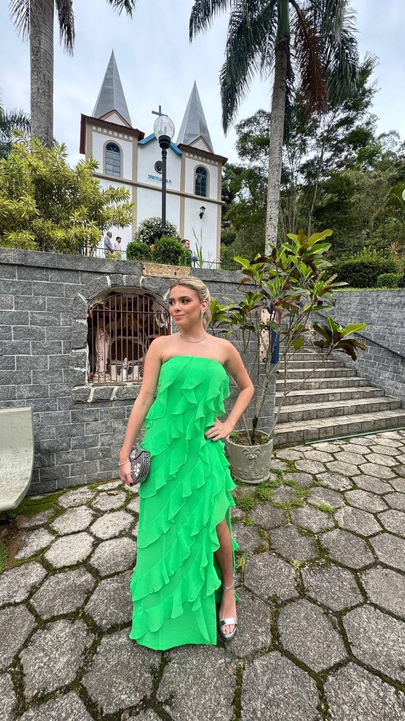 Vestido longo verde com camadas de babados, decote tomara que caia, caimento fluido e fenda lateral.