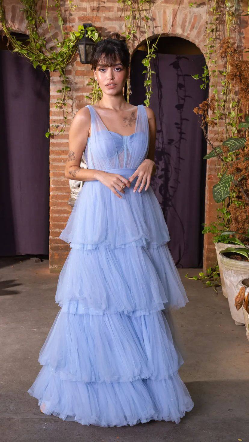 Vestido longo azul claro de tule, com corpete estruturado, decote V e saia volumosa em camadas.
