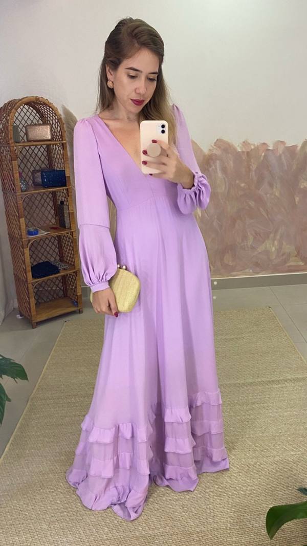 Vestido longo lilás com decote V, mangas longas bufantes, caimento fluido e detalhe de babados na barra.