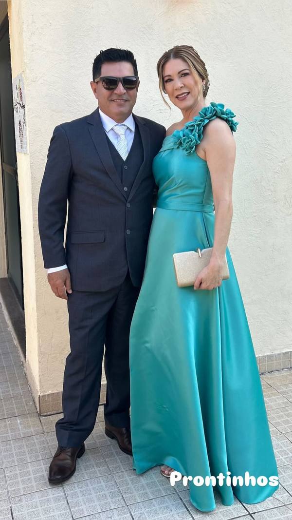 Vestido longo verde de cetim, modelo um ombro com aplicações de flores na alça e saia evasê.