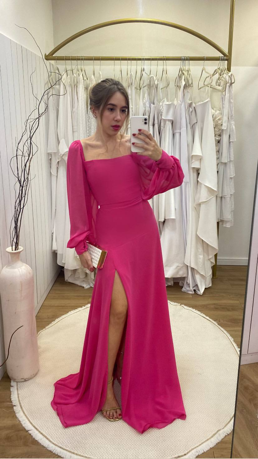 Vestido longo fúcsia de manga longa, decote quadrado, saia levemente evasê com fenda frontal.