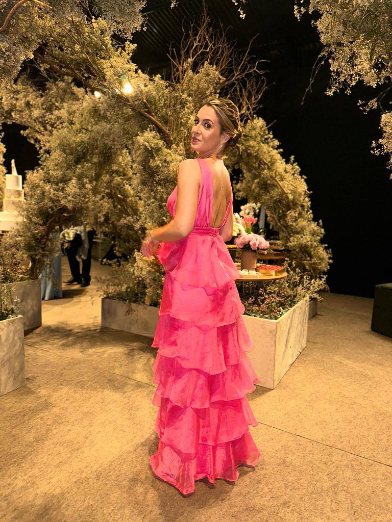 Vestido longo fúcsia com decote nas costas, saia fluida em camadas de babados e alças largas.