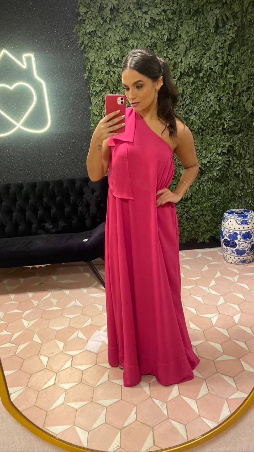 Vestido longo fúcsia de caimento fluido, com decote de um ombro só e tecido leve.