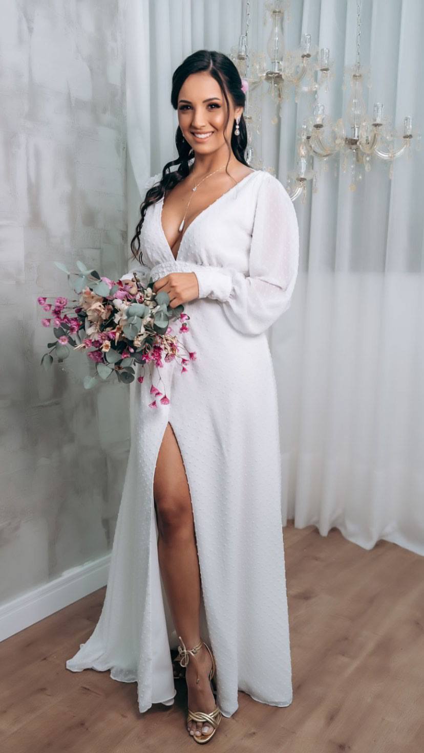 Vestido longo branco com mangas longas, decote V profundo, fenda frontal e caimento fluido.