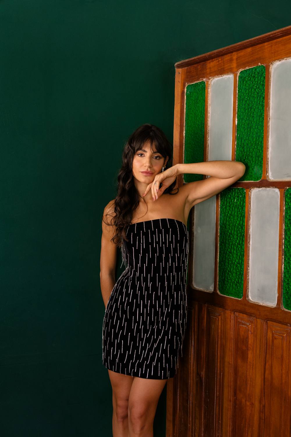 Vestido curto preto tomara que caia, com caimento reto e aplicação de brilhos em linhas verticais.