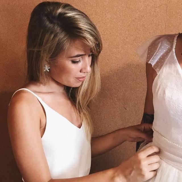 Amanda Magalhães ajustando o vestido de uma noiva no ateliê
